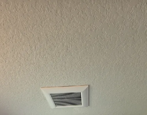 Bathroom exhaust fan grille installed in a textured ceiling