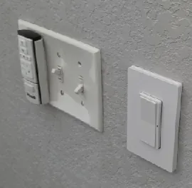 Ceiling fan wall control and toggle switches beside a new decorator dimmer
