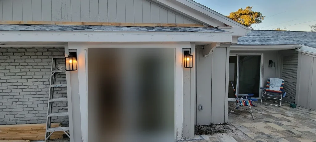 Outdoor & Landscape Lighting for Pinellas Homes: A Homeowner's Planning Guide Two black lantern-style coach lights lit at dusk on either side of a new sliding glass door opening onto a paver patio at a Pinellas County home