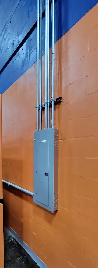 Commercial panelboard with EMT conduit risers on a painted block wall