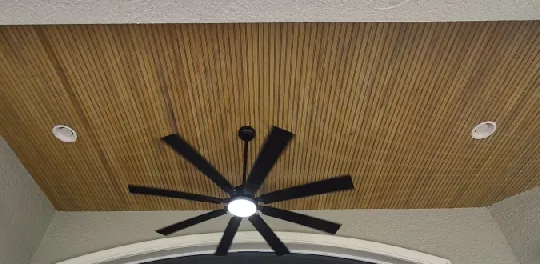 Eight-blade black ceiling fan with an LED light and recessed lights on a wood porch ceiling