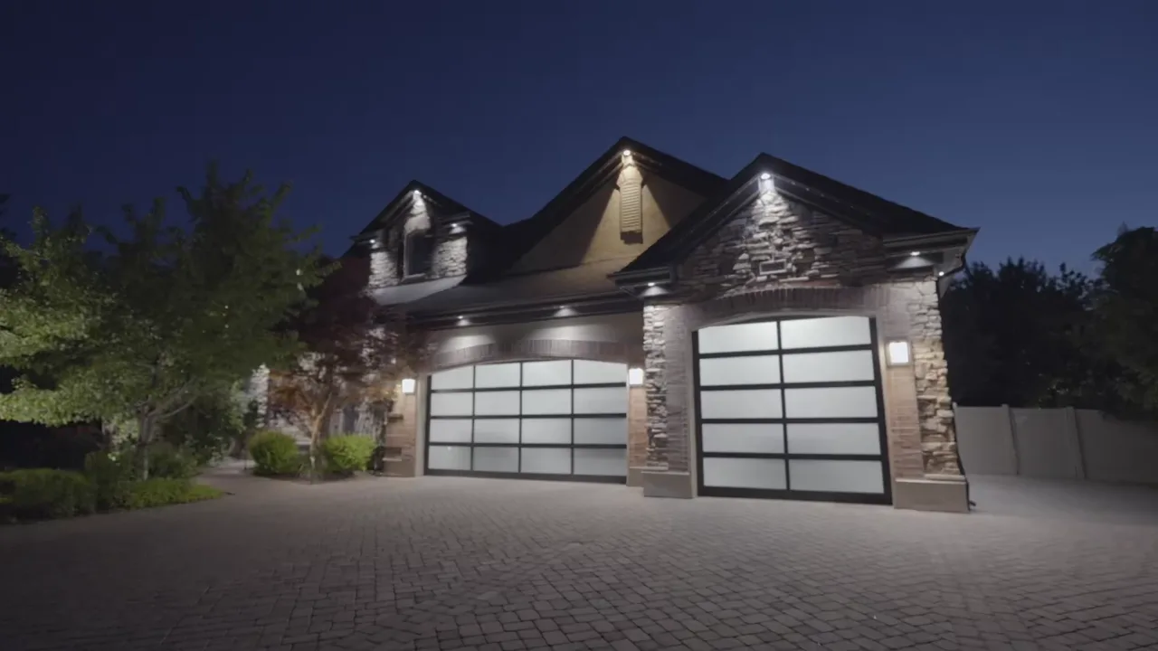 Stone-front home with bright white JellyFish Lighting downlight over the garage doors and driveway at night