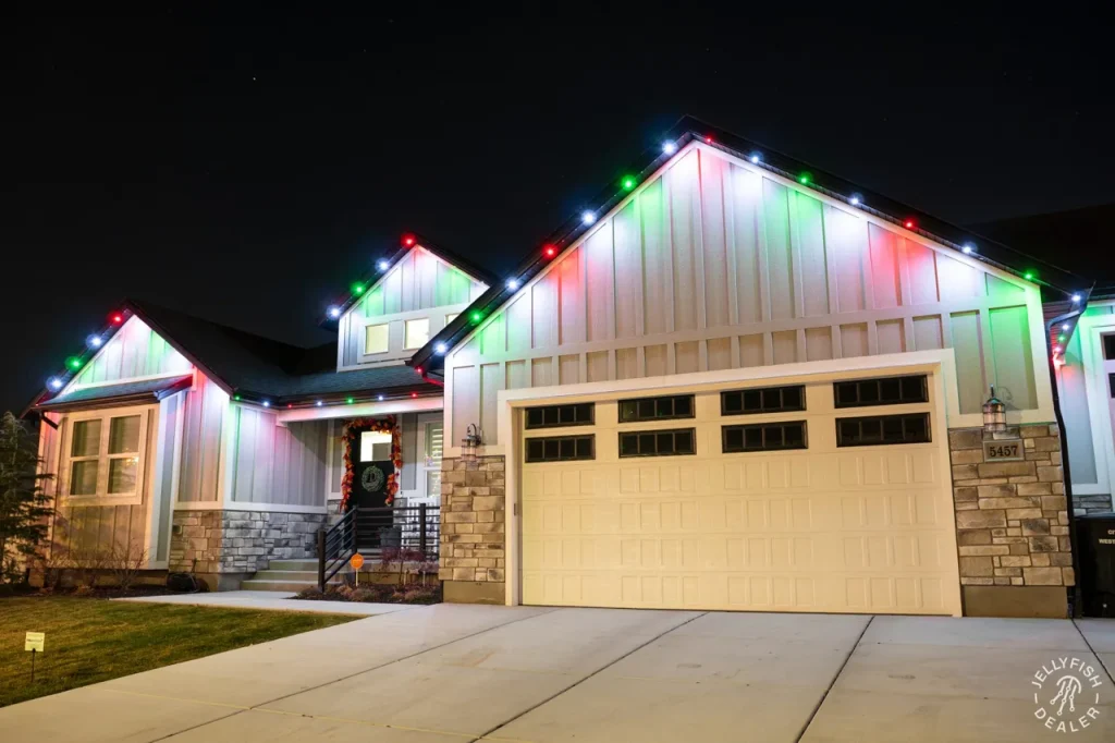 Wide single-garage home with red, white and green JellyFish permanent Christmas lights on the roofline