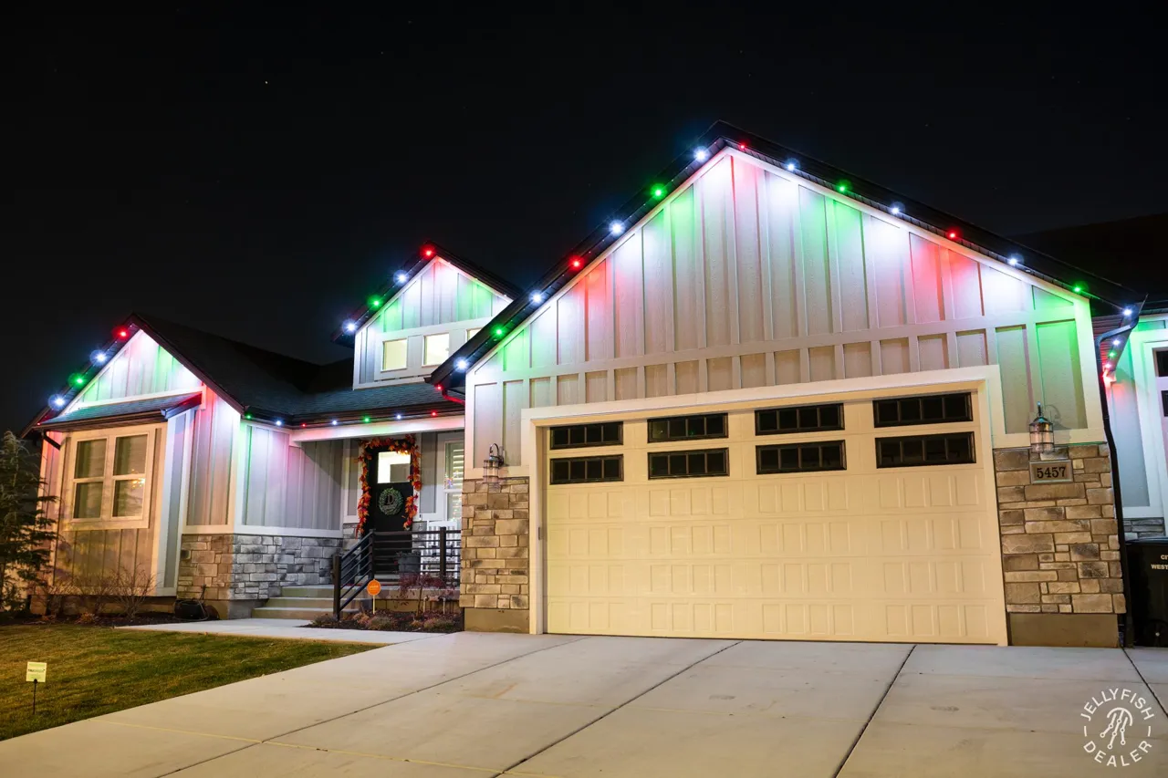 Wide single-garage home with red, white and green JellyFish permanent Christmas lights on the roofline