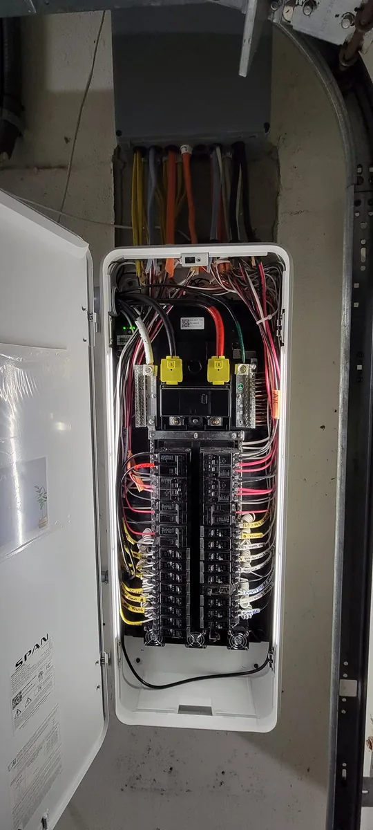 SPAN smart panel installation in progress with the SPAN-branded door open and new conduit above, Tampa Bay area