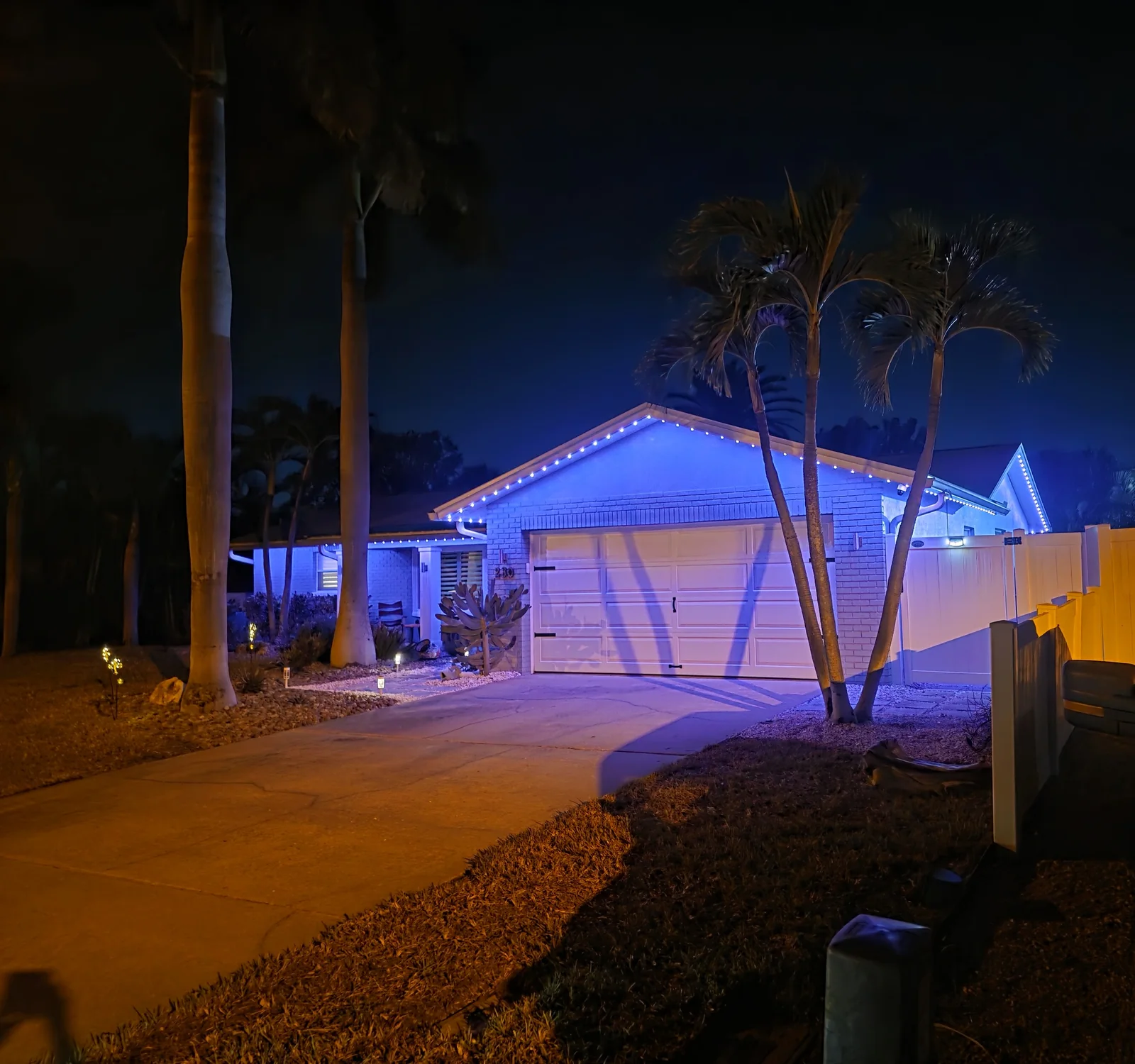 Same Tampa Bay home at night with JellyFish permanent lights glowing blue under the eaves over the garage