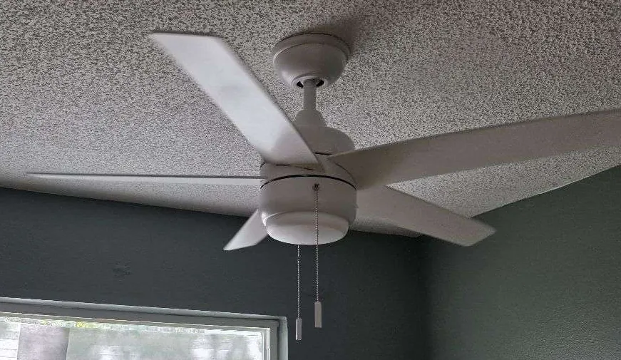 White ceiling fan with light kit and pull chains on a textured ceiling
